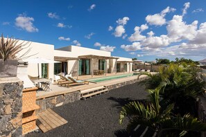A modern villa with a pool, outdoor seating, and a stone wall.