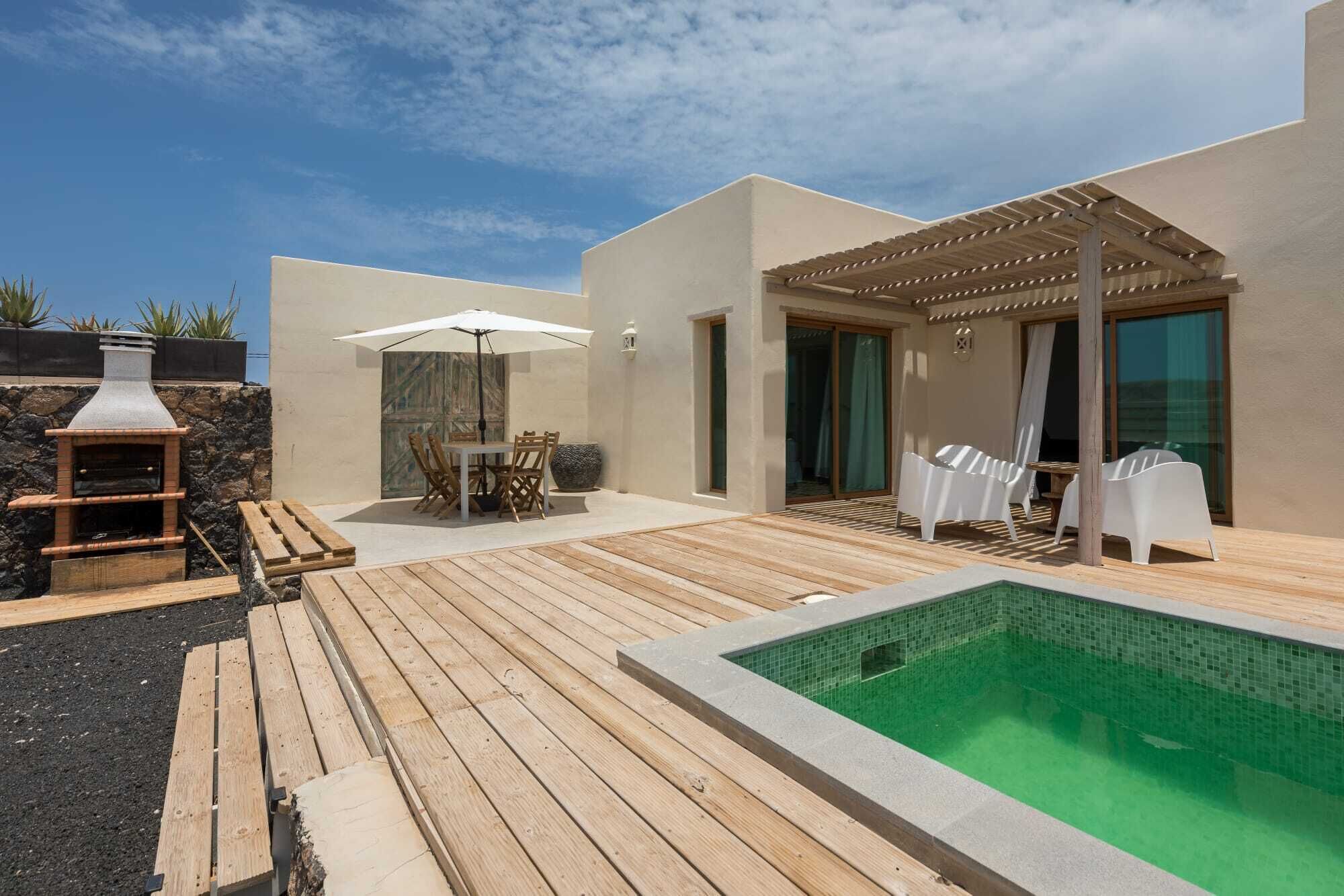 A modern outdoor pool area with a wooden deck, a stone wall, and a pergola.