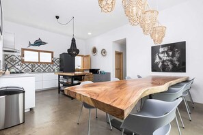 A modern kitchen with a wooden dining table, grey chairs, a hanging light fixture, and a wall-mounted fish decoration.