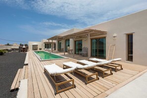Zona de piscina en la azotea con sillones de descanso, una pérgola y vistas al mar.