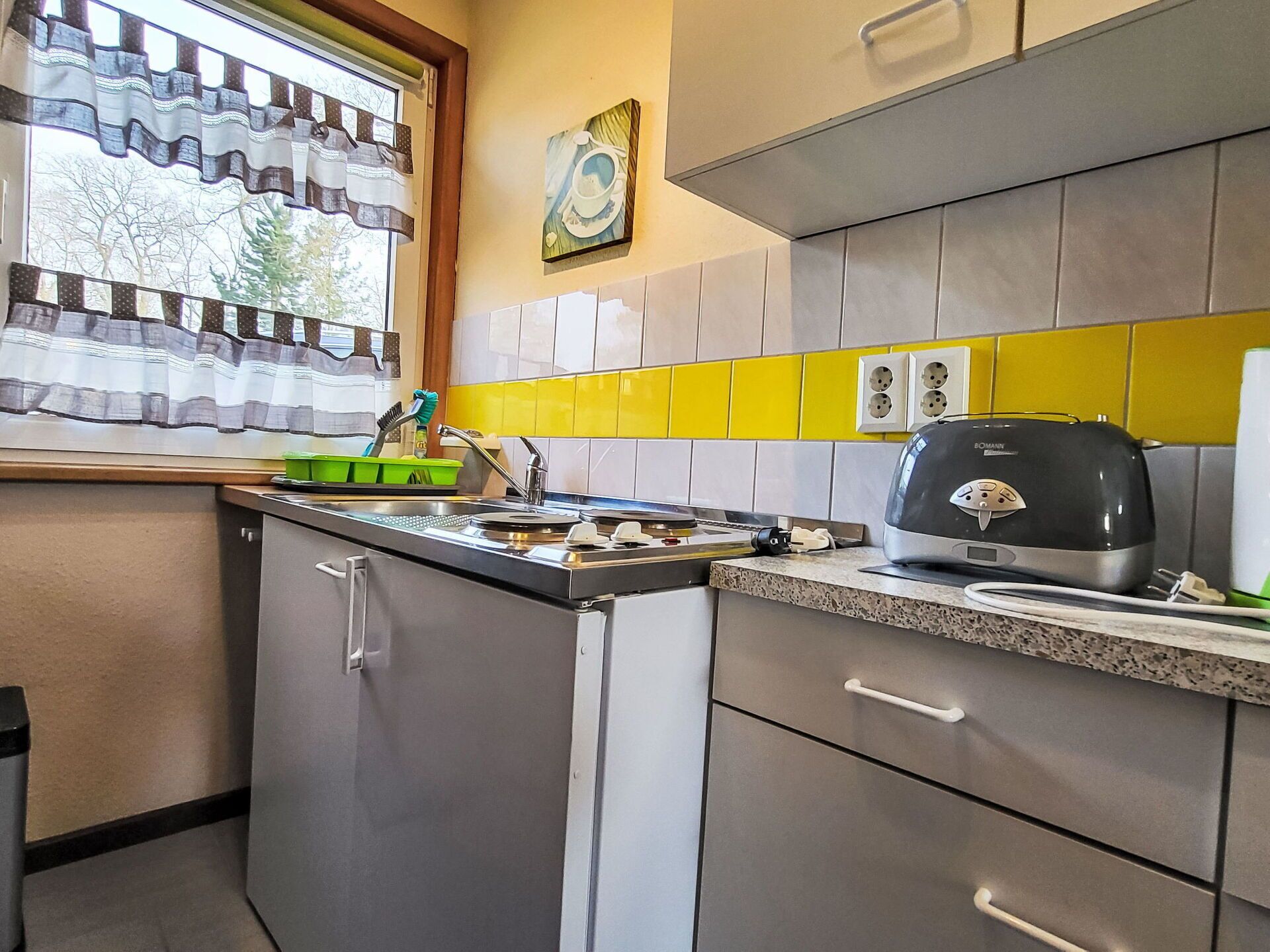 Una cucina con lavastoviglie integrata, un tostapane e una finestra con tende a motivi.