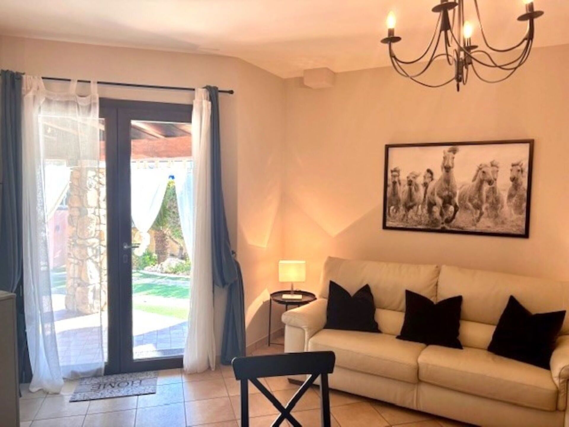 A living room with a sofa, a chair, a table, a chandelier, and a door leading outside.