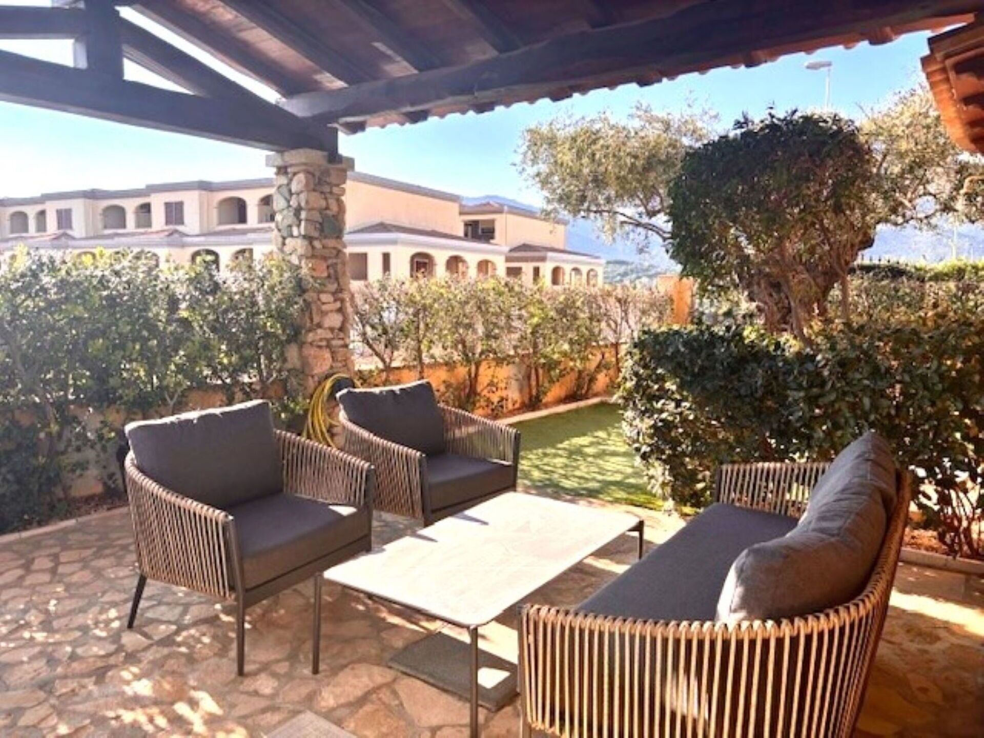 An outdoor patio with wicker furniture, a stone pillar, and a view of a building with arches.