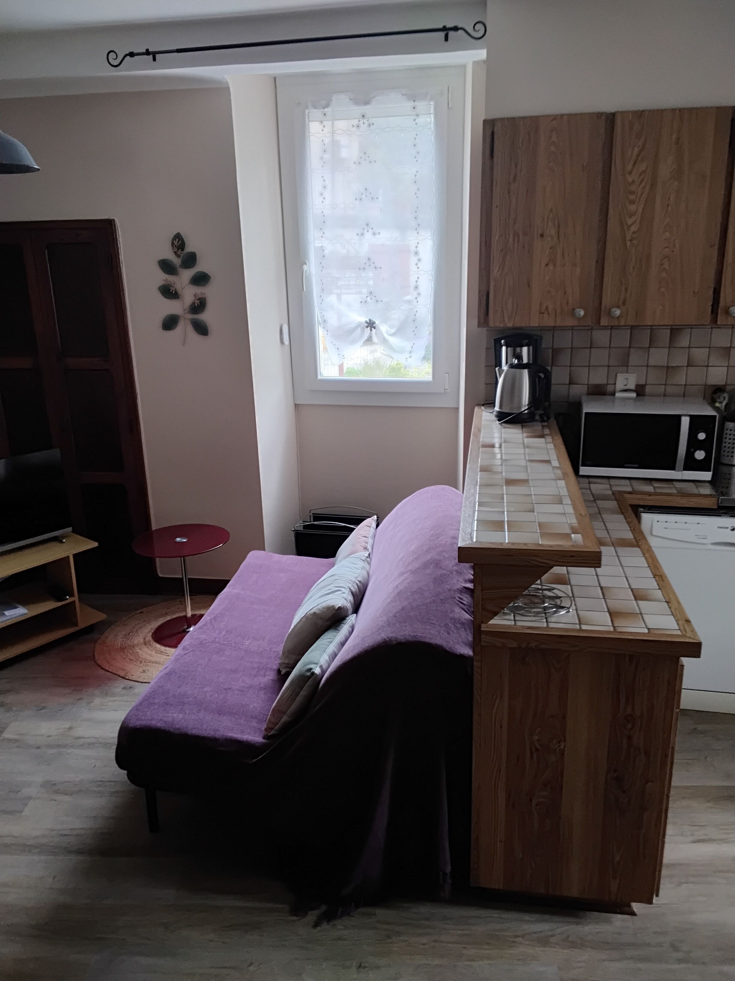 Une pièce de taille modeste comprenant un lit, un coin cuisine, une fenêtre avec des rideaux et une petite table.