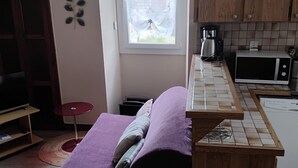 Een compacte kamer met een bed, een kitchenette, een raam met gordijnen en een klein tafeltje.