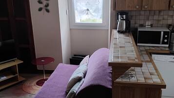 Une pièce de taille modeste comprenant un lit, un coin cuisine, une fenêtre avec des rideaux et une petite table.