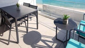 Ein Balkon mit Meerblick, einem Tisch mit Stühlen und einem kleinen, runden Tisch mit einer Pflanze.