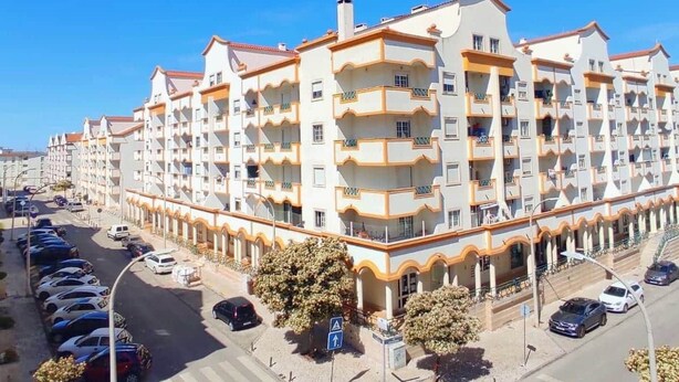 Un immeuble résidentiel à plusieurs étages, doté de balcons, d’un parking et surplombant un ciel dégagé.
