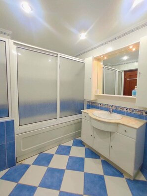 A bathroom with a checkered floor, a sink, a mirror, and a shower enclosure. - The Golden Hour Retreat (Alcochete)