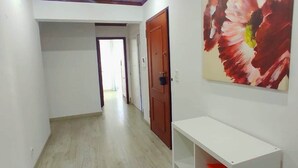 Un couloir avec un plafond en bois, un mur blanc orné d’un grand tableau représentant des fleurs et une étagère blanche remplie de livres.