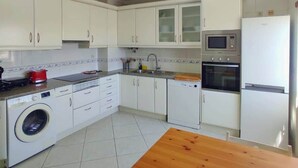 Une cuisine compacte avec des meubles blancs, un lave-linge, un four à micro-ondes et un réfrigérateur.