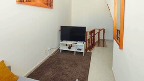 Une chambre à coucher avec un lit, un téléviseur posé sur un meuble, un tableau accroché au mur et un escalier.