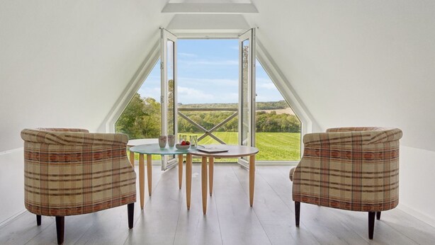 A room with a high ceiling, a table with chairs, and a large window offering a view of the countryside. - "Sigbritt" - 3.7km from the sea by Interhome (Nexø)