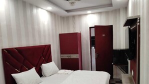 Egy szállodai szoba, amelyben található egy ágy, egy szekrény, egy tükör és egy mennyezeti ventilátor.