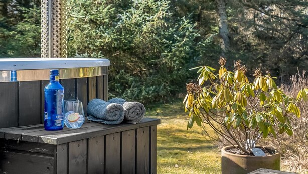 Ein Whirlpool mit Metallstab, einer blauen Flasche, einem Glas und Handtüchern auf einer Holzdielenfläche.