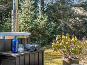 Ein Whirlpool mit Metallstab, einer blauen Flasche, einem Glas und Handtüchern auf einer Holzdielenfläche.