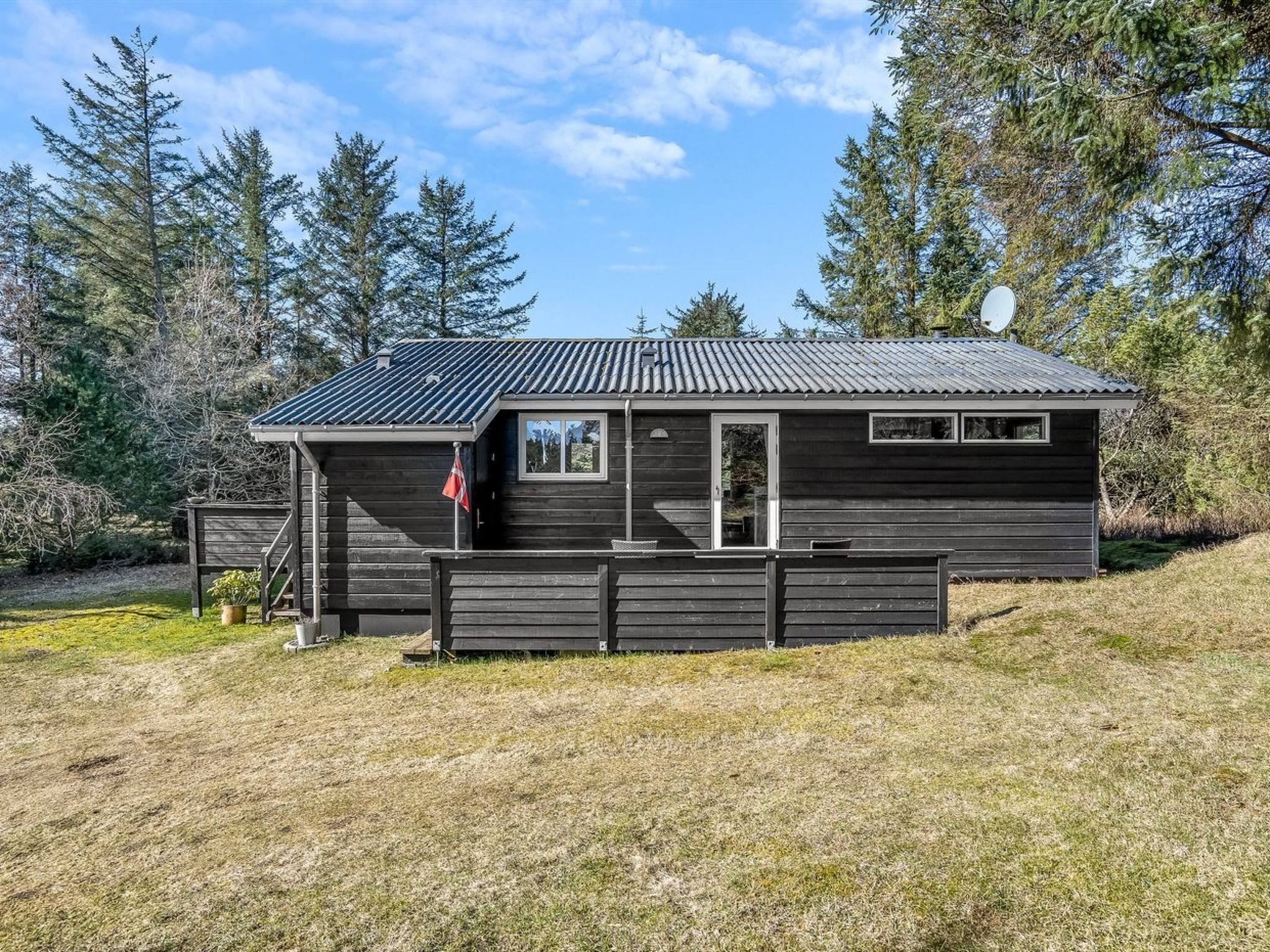 A small cabin with a metal roof, a wooden deck, and a satellite dish.