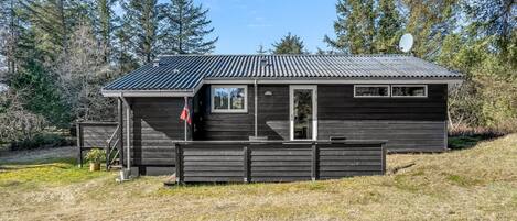 A small cabin with a metal roof, a wooden deck, and a satellite dish.