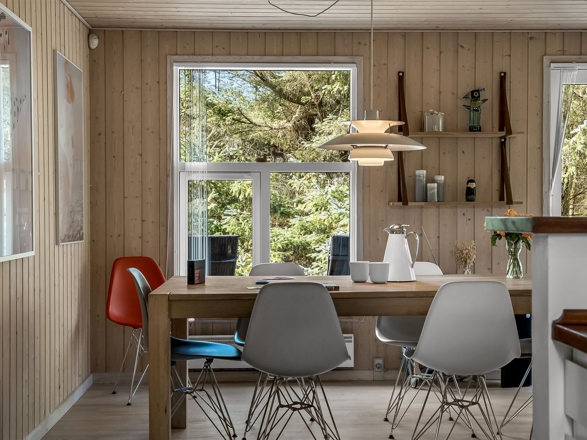 Moderni keittiö, jossa on puuseinät, suuri ikkuna sekä ruokailutila, jossa on tuoleja ja pöytä.