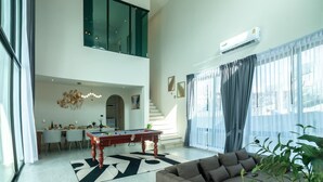 Ein modernes Wohnzimmer mit Billardtisch, einer Couch und einer Treppe, die in eine obere Etage führt.