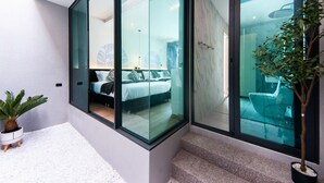 Ein modernes Schlafzimmer mit einer Glaswand, einem Bett, einer Pflanze und einem Badezimmer mit Badewanne.