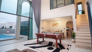 Ein modernes Interieur mit Billardtisch, großen Fenstern und einer Treppe.