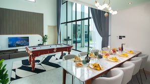 Ein modernes Wohnzimmer mit Billardtisch, Essbereich und großen Fenstern.