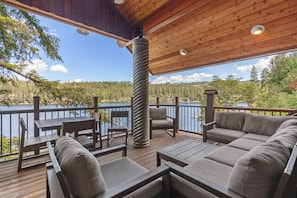 A covered deck with outdoor furniture, a view of a lake, and a forested landscape. - New Listing! Lakefront | Spacious Deck | Private Dock | Hot Tub | Tram (Harrison)