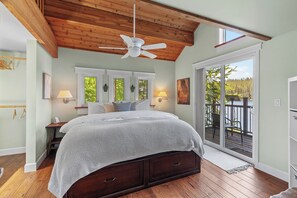 A bedroom with a wooden ceiling, a bed with a white blanket, two bedside lamps, and a view of a deck through a sliding glass door. - New Listing! Lakefront | Spacious Deck | Private Dock | Hot Tub | Tram (Harrison)