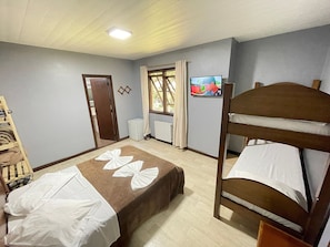 A hotel room with a bunk bed, a single bed, a television, a window with curtains, a radiator, and a wooden ladder. - Pousada Bella Serra (Canela)
