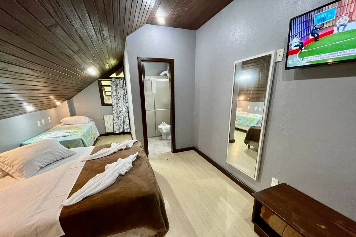 Un dormitorio con dos camas, televisión, espejo y techo de madera.