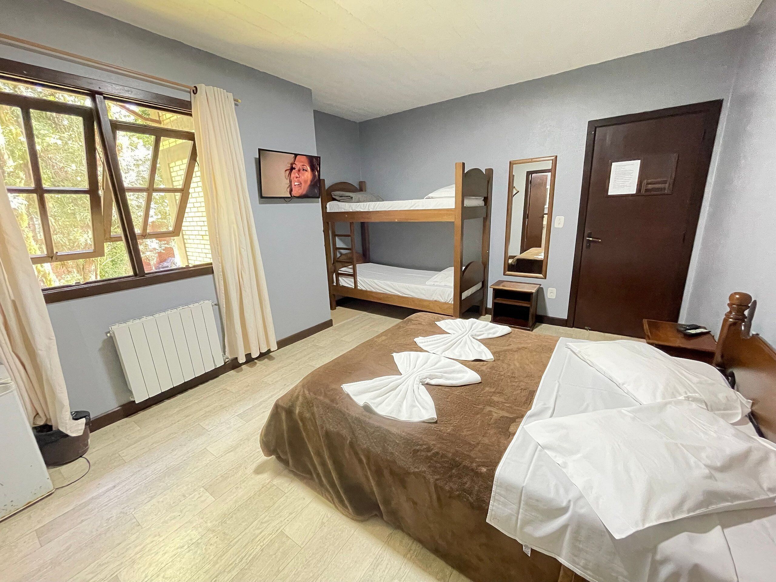 A room with a bunk bed, a small table, a mirror, a radiator, and a window with curtains.