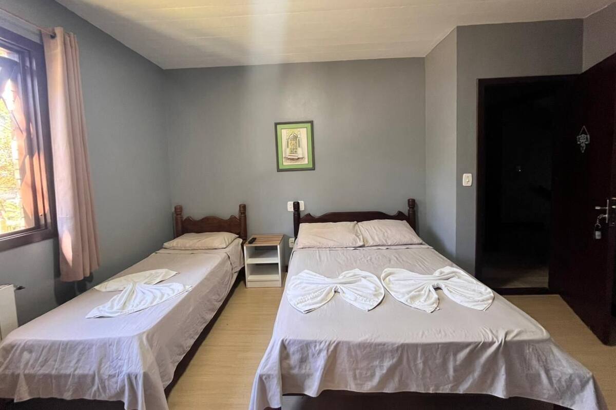 Una habitación con dos camas individuales, una mesita de noche, un cuadro enmarcado en la pared y una puerta que da a otra estancia.