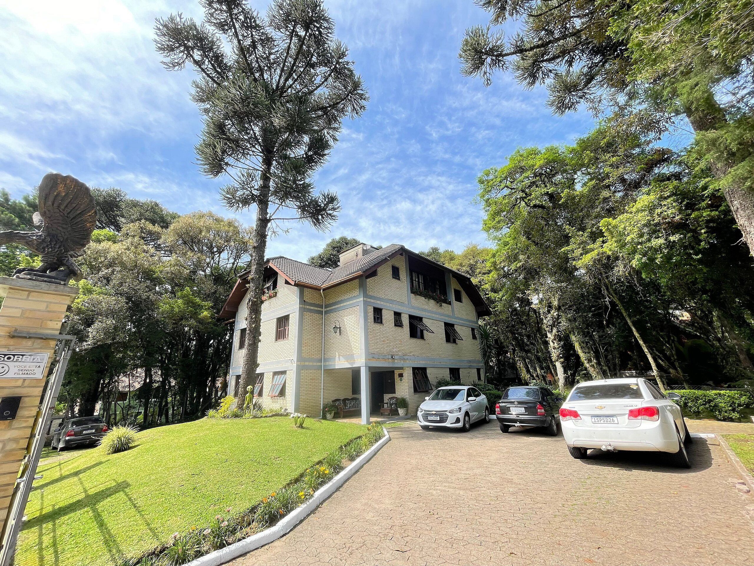 Un edificio de dos pisos con techo de tejas, rodeado de árboles y automóviles estacionados.