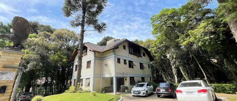 A two-story building with a tiled roof, surrounded by trees and parked cars.