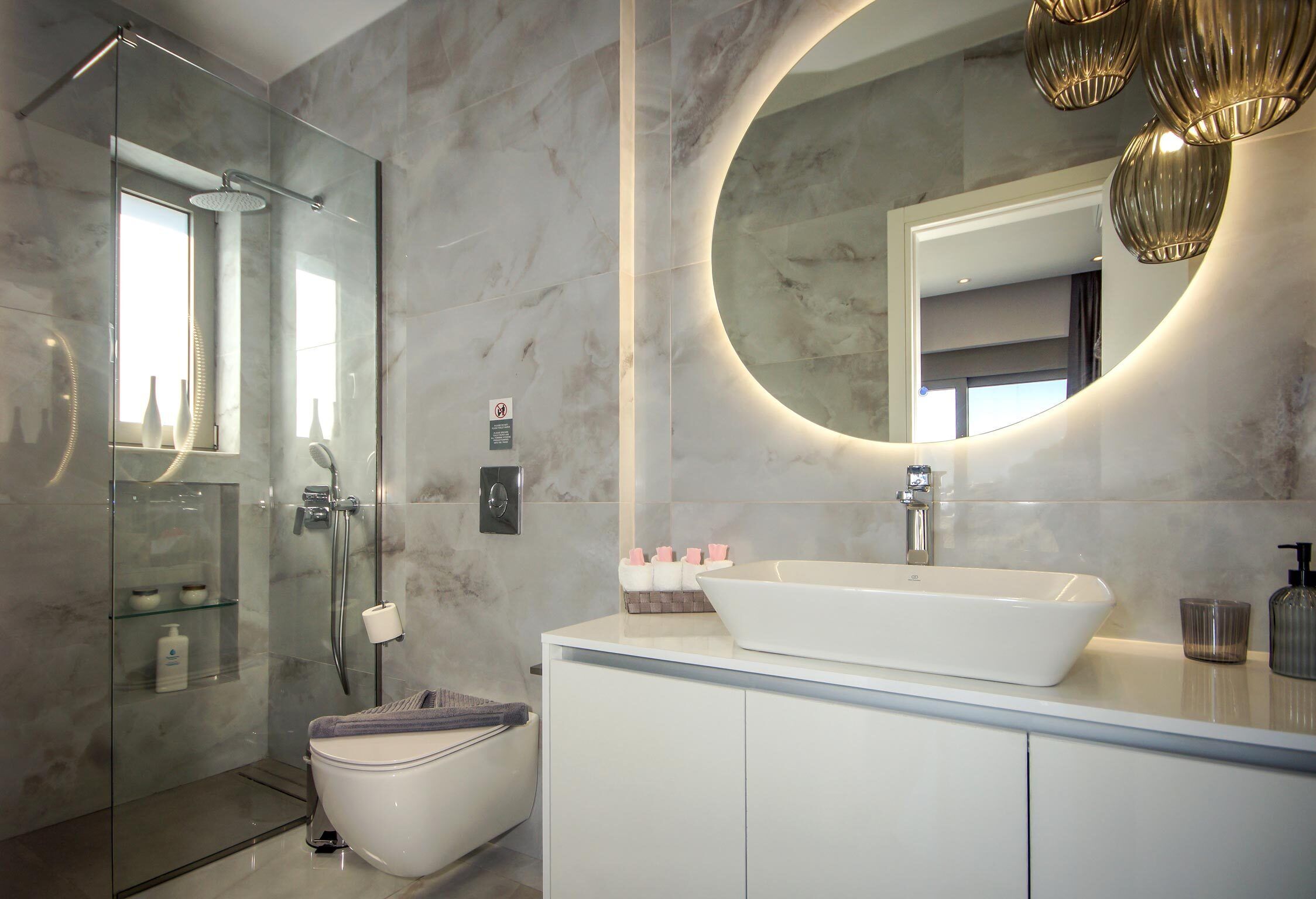 A modern bathroom with a glass-enclosed shower, a white sink, and a large mirror with a circular frame.