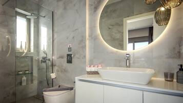 A modern bathroom with a glass-enclosed shower, a white sink, and a large mirror with a circular frame.