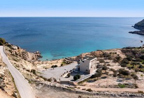 A coastal building with a paved area, a winding road, and a view of the sea. - Villa Aquamarine beachfront Rhodes (Stegna)
