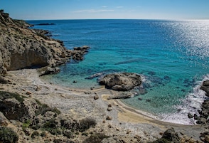 Una playa rocosa con aguas azules cristalinas y un litoral escarpado.