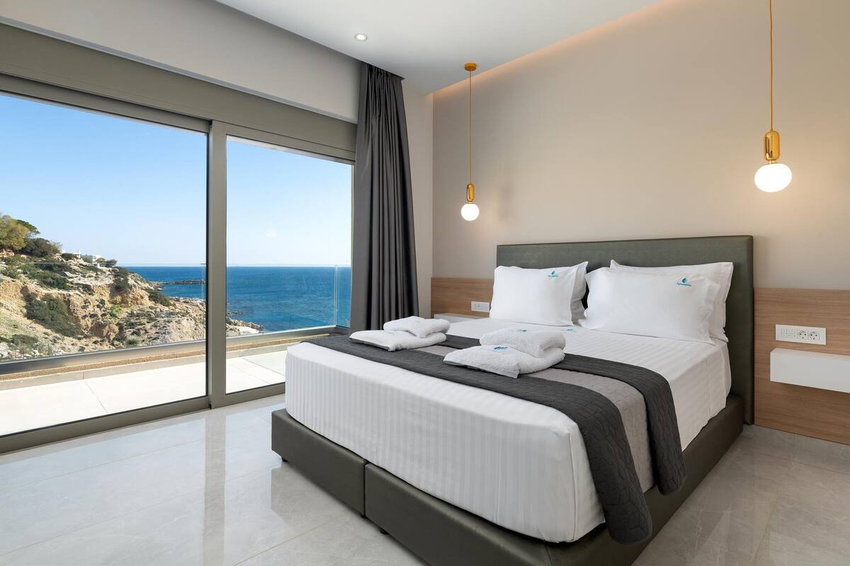 A modern hotel room with a large bed, a view of the sea, and a balcony.