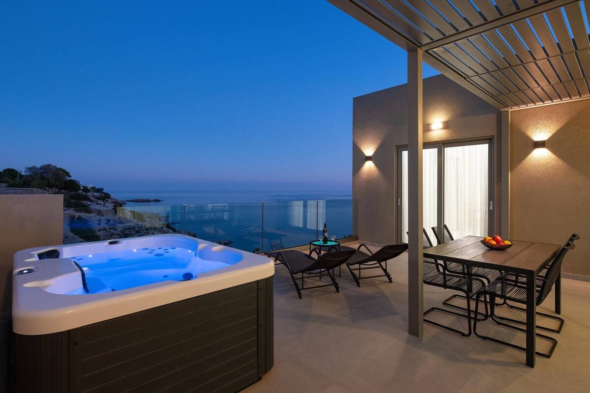 A hot tub on a balcony with a table and chairs, overlooking a body of water.