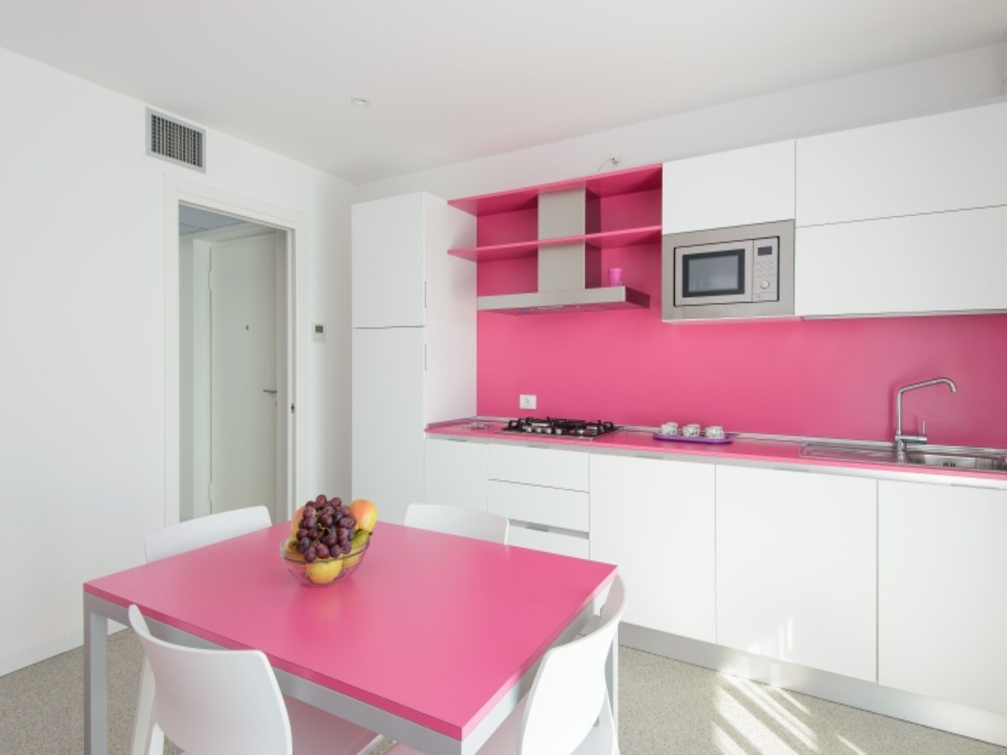 Een moderne keuken met witte kasten, een roze aanrecht en een magnetron.