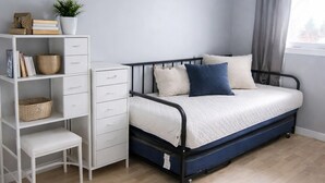 A bedroom with a bed, a white dresser, a small table, a ceiling fan, and a window with curtains.