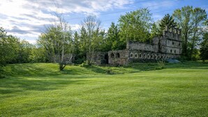 An old stone building with arched windows and a grassy field in the foreground.