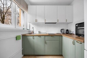 Eine kleine Küche mit weißen Oberschränken, grünen Unterschränken, einer Holz Arbeitsplatte und einem schwarzen Backofen.