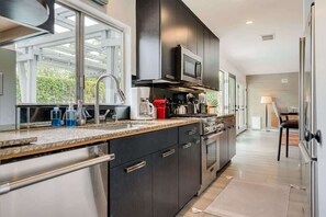 A modern kitchen with dark cabinets, stainless steel appliances, and a large window providing natural light. - Mid-century Oasis w Private Pool Mountain Views (Rancho Mirage)