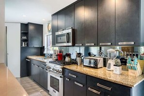 A modern kitchen with dark cabinetry, stainless steel appliances, and a granite countertop. - Mid-century Oasis w Private Pool Mountain Views (Rancho Mirage)
