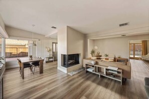 A modern living room with a fireplace, wooden flooring, a dining area, and a sofa. - Zen Palm Desert Bungalow (Palm Desert)