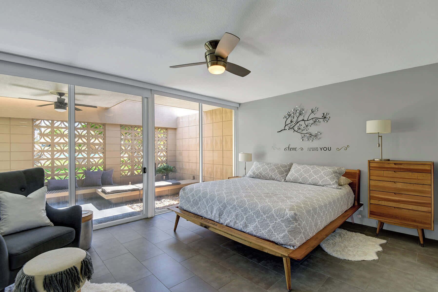 A bedroom with a bed, a wooden dresser, a ceiling fan, a wall art piece, and a sliding glass door leading to an outdoor area.