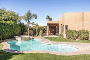 A swimming pool with a curved design, surrounded by a well-maintained lawn and palm trees. - Desert Dreamhouse 4BR Pool Spa (Palm Desert)